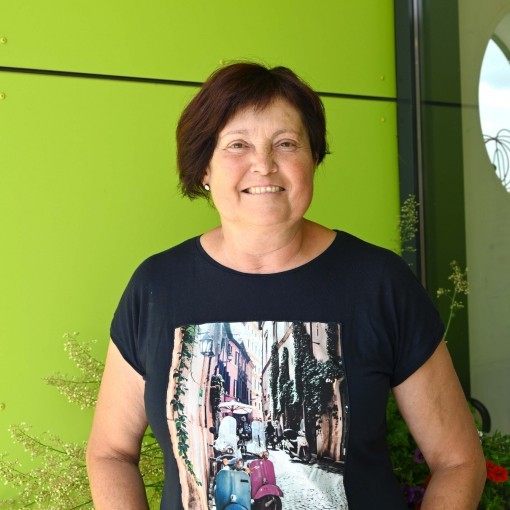 Frau mittleren Alters in einem schwarzen T-Shirt mit einem Bild einer Vespa auf einer Kopfsteinpflasterstraße.