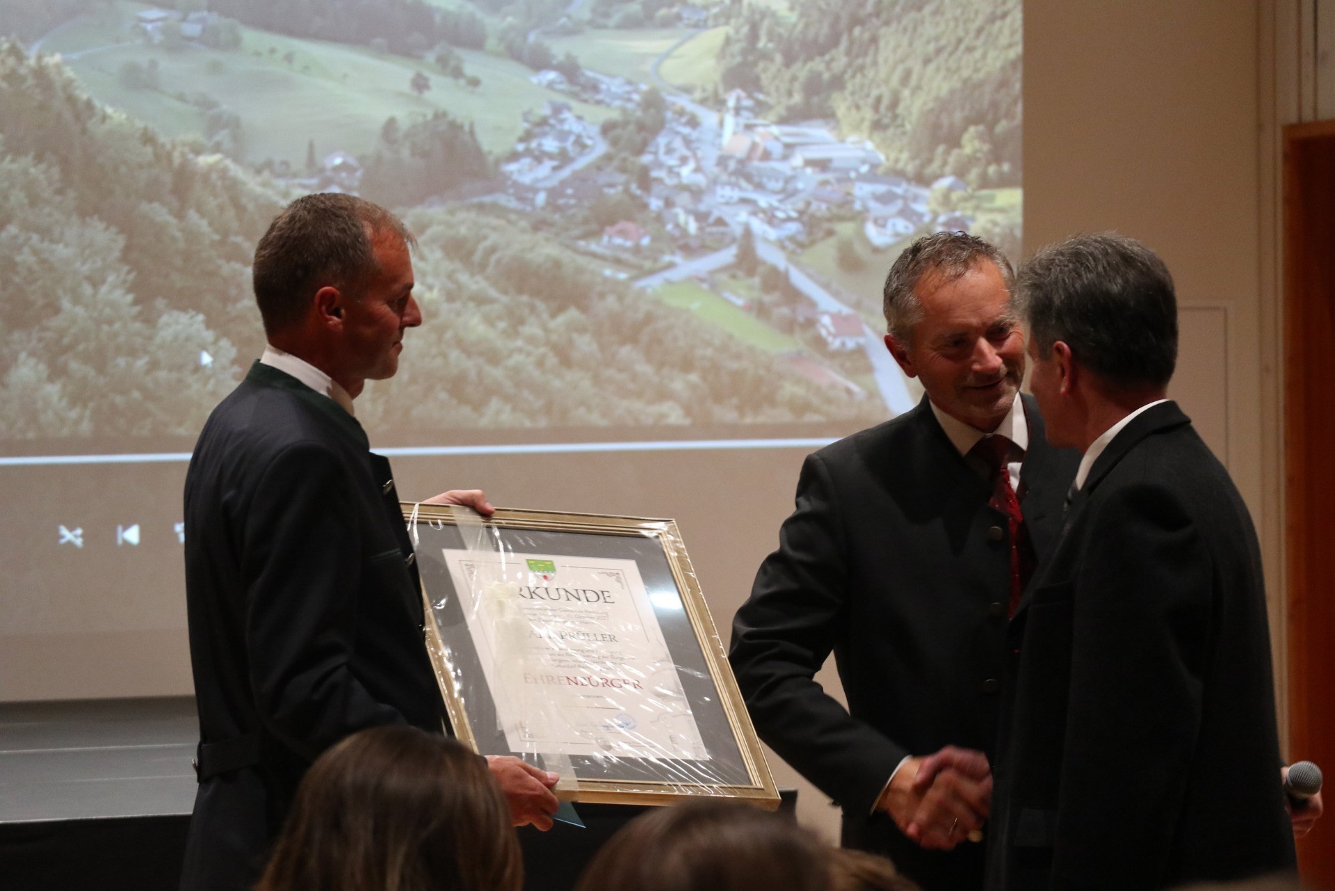 Zwei Männer schütteln Händchen, wobei einer ein Zertifikat überreicht bekommt.