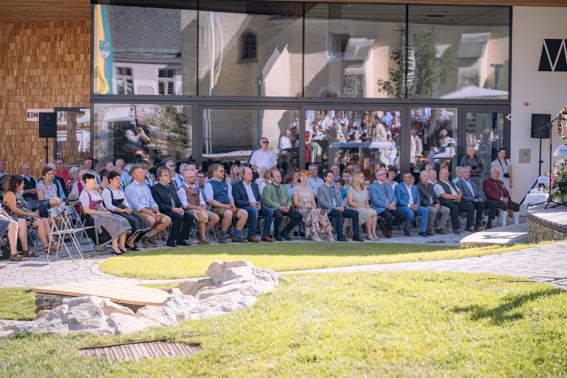 Sitzende Personen auf einer Bank vor einem Gebäude. Versammlung im Freien.