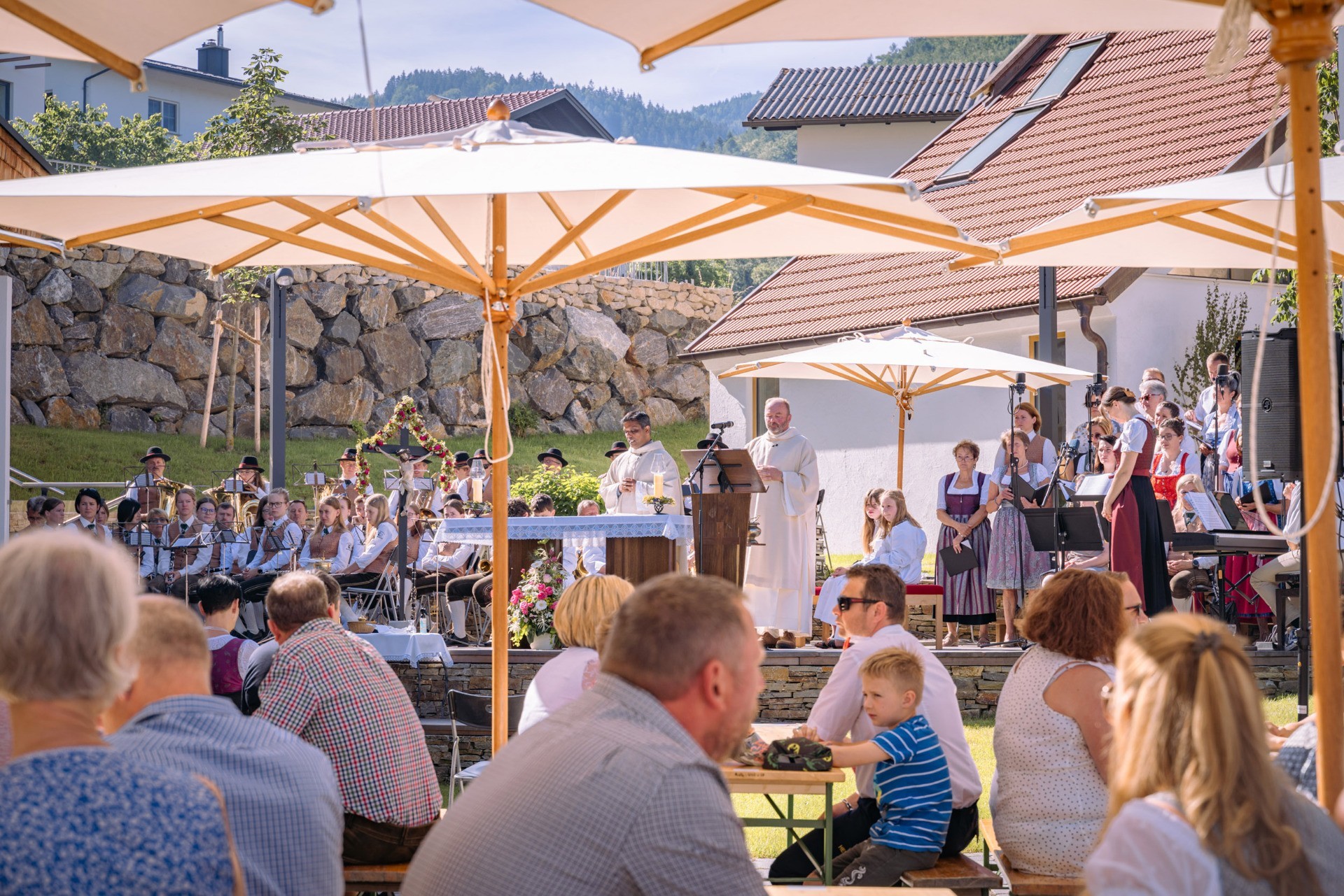 Gemütliches Fest mit Musikern und Gästen unter einem Sonnensegel. Eine Bühne mit Redner und Musikern im Grünen.