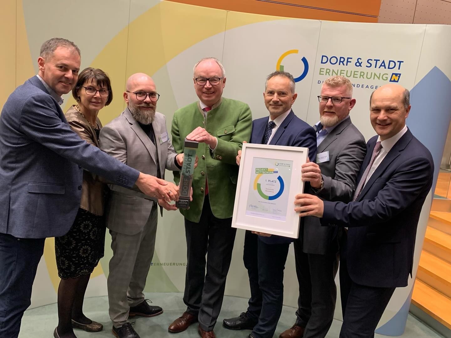 Mehrere Männer halten einen Umweltpreis in den Händen. Der Preis zeigt ein grünes Blatt und einen Kreislauf, umweltbezogen.