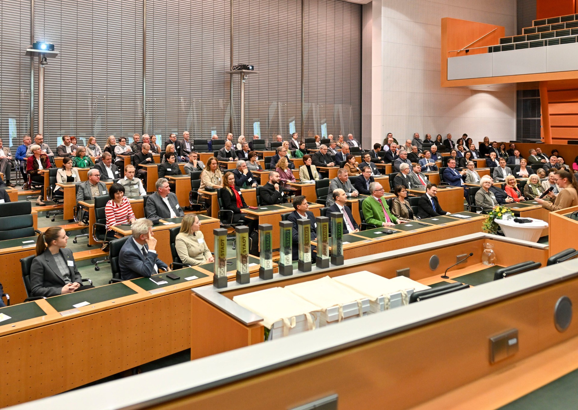 Versammlung in einem Sitzungssaal mit vielen Menschen, die an Tischen sitzen.