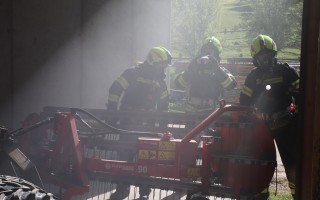 Zwei Feuerwehrleute in Schutzanzügen stehen vor einem gelben Traktor. Im Hintergrund verschwommenes Grün.