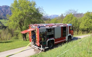 Rotes Feuerwehrauto in ländlicher Umgebung, am Straßenrand, mit Gelbstreifen. Hügelige Landschaft im Hintergrund.