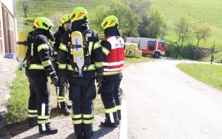 Mehrere Feuerwehrleute in Schutzanzügen stehen eng beieinander, vermutlich bei einer Diskussion oder Planung. Im Hintergrund ist ein roter Feuerwehrfahrzeug sichtbar.