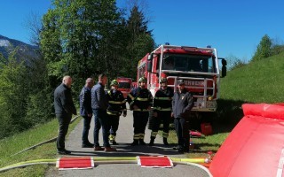 Feuerwehrbesatzung bespricht vor einem roten Tanklöschfahrzeug auf einem Feld.