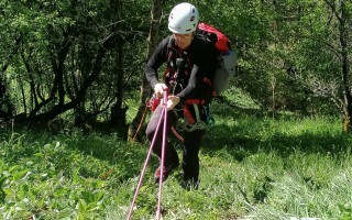 Kletterer mit Sicherungsausrüstung hängt an einer Seilbahn in einem Waldstück.