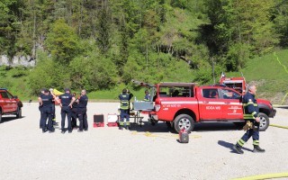 Feuerwehrleute arbeiten an einem roten Fahrzeug, vermutlich ein Abschleppfahrzeug, auf einem Parkplatz.