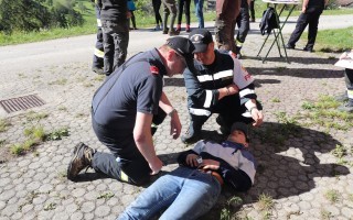 Personen überprüfen Zustand eines Bewusstlosen auf einem Feldweg. Zwei Helfer untersuchen einen Mann, der auf dem Boden liegt.