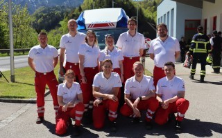 Eine Gruppe von Einsatzkräften in rot-weißen Uniformen posiert vor einem weißen Krankenwagen.