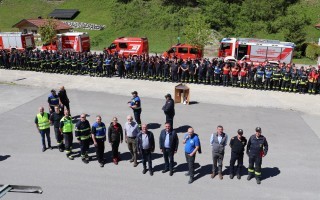 Versammlung von Feuerwehrleuten und Beamten vor einem roten Feuerwehrauto.