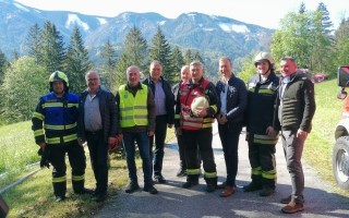 Feuerwehrleute in Schutzkleidung und Warnwesten stehen auf einem Straßenabschnitt. Im Hintergrund verschneite Berge.