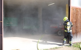Feuerwehrmann mit Atemschutzgerät und Schlauch in einem geschützten Bereich, Hintergrund: Garage mit Geländer.