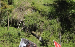 Feuerwehrfahrzeug im Vordergrund, umgeben von dichten Bäumen und einer steilen Hanglandschaft im Hintergrund.