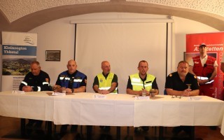 Versammlung von Personen um einen Tisch, Banner im Hintergrund, vermutlich ein Arbeitskreis oder Team.