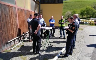 Mehrere Männer stehen in einem Gespräch um einen stabilen Ständer. Im Hintergrund ein grauer Holzzaun.