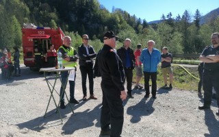 Feuerwehrleute diskutieren an einem Holztisch an einem Feld. Im Hintergrund steht ein Feuerwehrauto.
