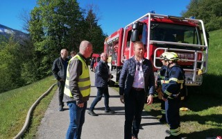 Feuerwehrleute besprechen am Rande eines Straßenabschnitts einen roten Feuerwehrfahrzeug.