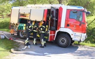 Rotes Feuerwehrfahrzeug mit zwei Einsatzkräften vor dem Fahrzeug. Auf dem Rückdeckel sind Schriftzüge zu sehen.
