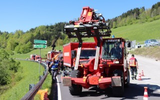 Roter Abschleppwagen blockiert Fahrbahn, Einsatzkräfte am Straßenrand.