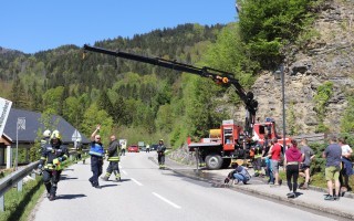 Straßenlage mit Einsatzkräften, darunter Feuerwehr, vor einem Einsatzfahrzeug. Im Hintergrund Berge.