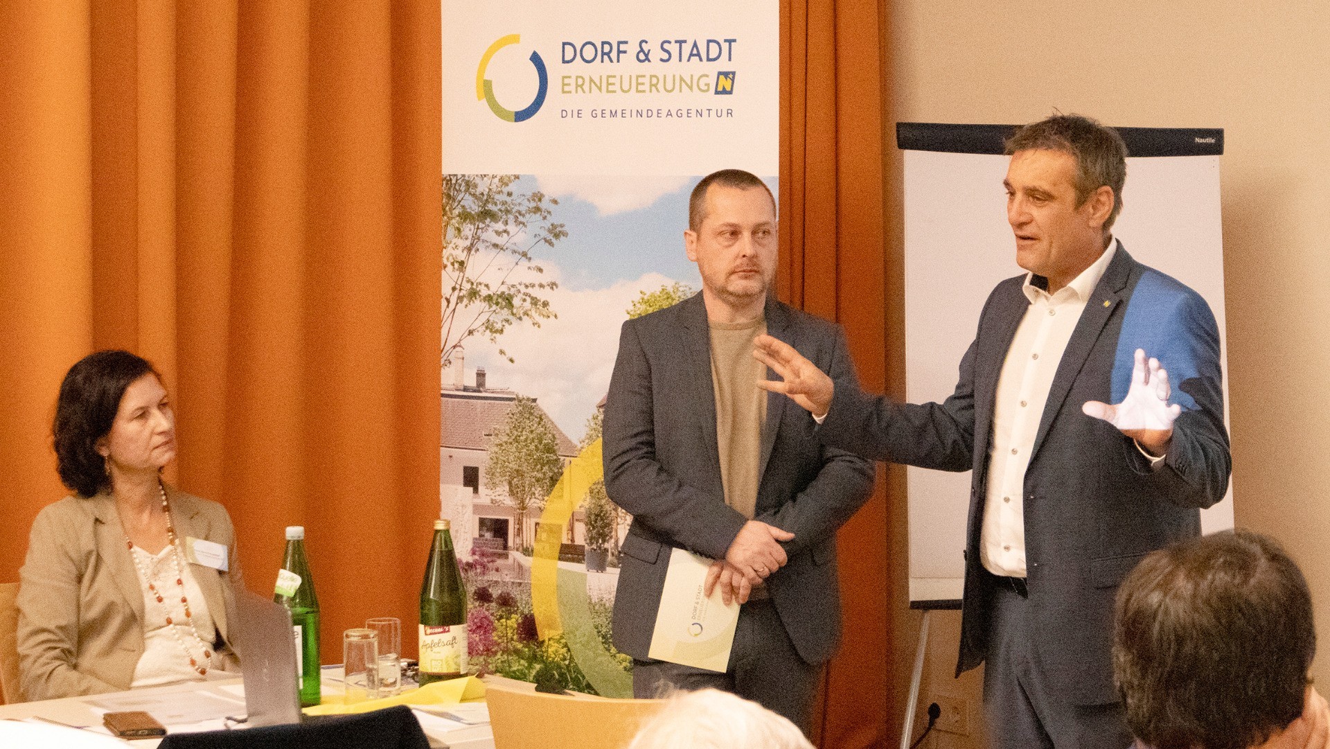 Ein Mann hält vor einem Hintergrundgespräch mit einer Frau. Auf dem Tisch stehen Getränke und ein Ordner.