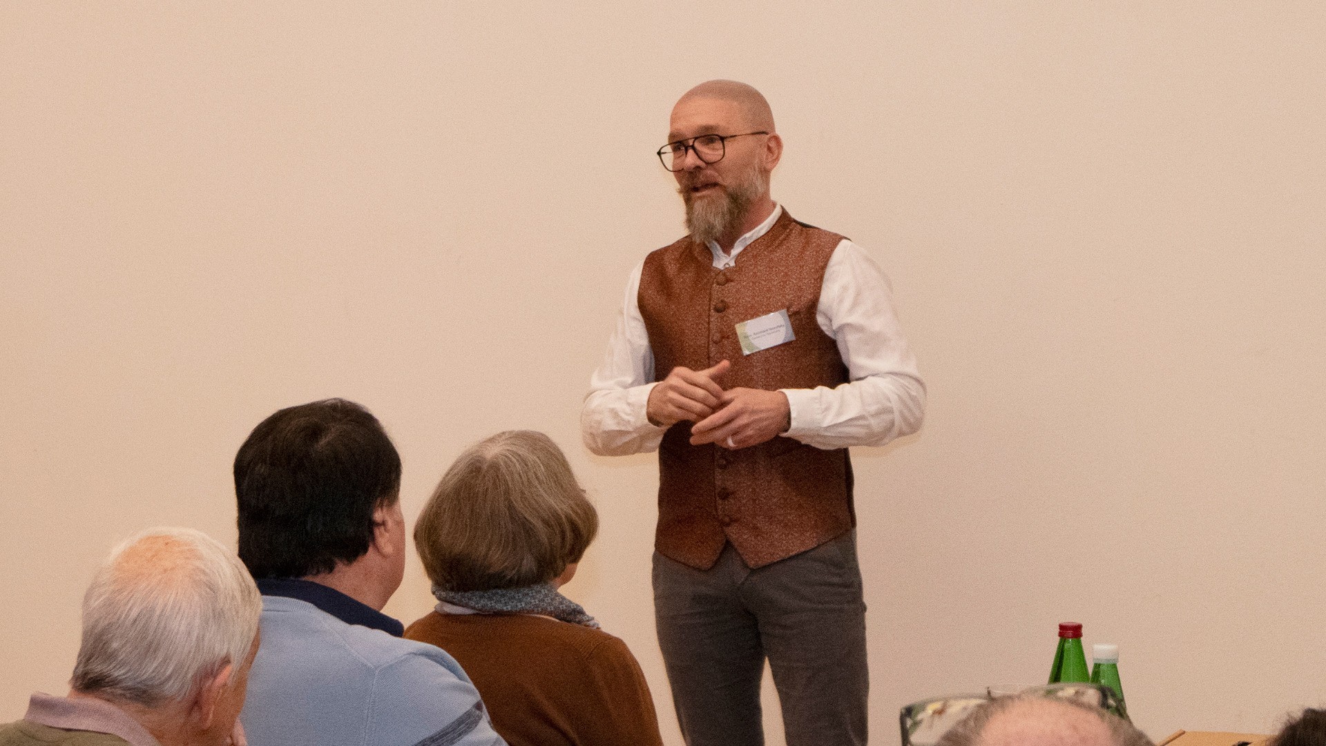 Mann spricht vor einer Gruppe von Menschen. Im Hintergrund sitzen weitere Personen.
