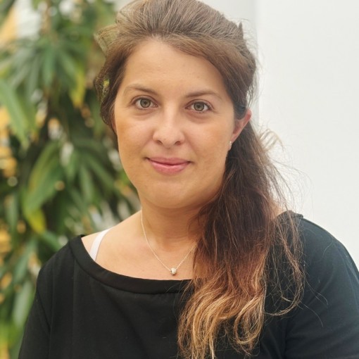Frau mit braunen, langen Haaren, die in eine schwarze T-Shirt gehüllt sind. Sie trägt eine silberne Halskette.