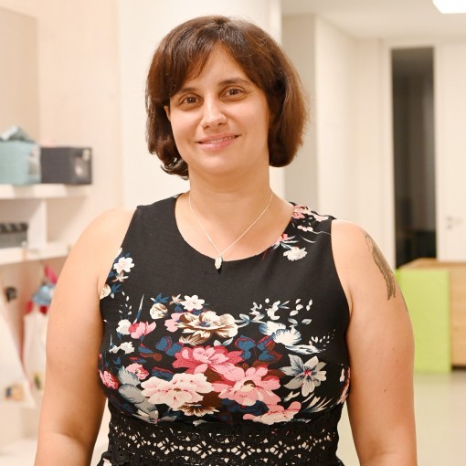 Frau in schwarzem Blätterkleid lächelt in die Kamera. Im Hintergrund ein weißer Raum mit Regalen.