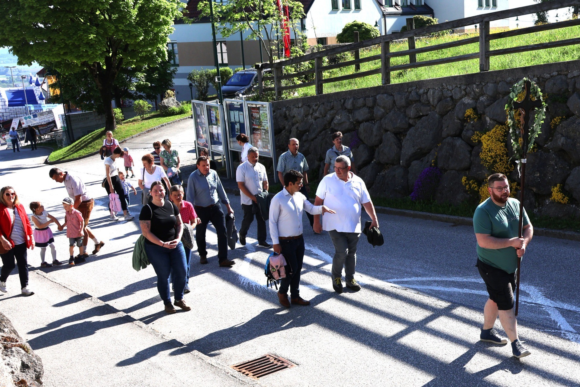 Eine Gruppe von Fußgängern geht einen Bürgersteig entlang, gespickt mit Kindern und Erwachsenen, im Schatten von Gittern.