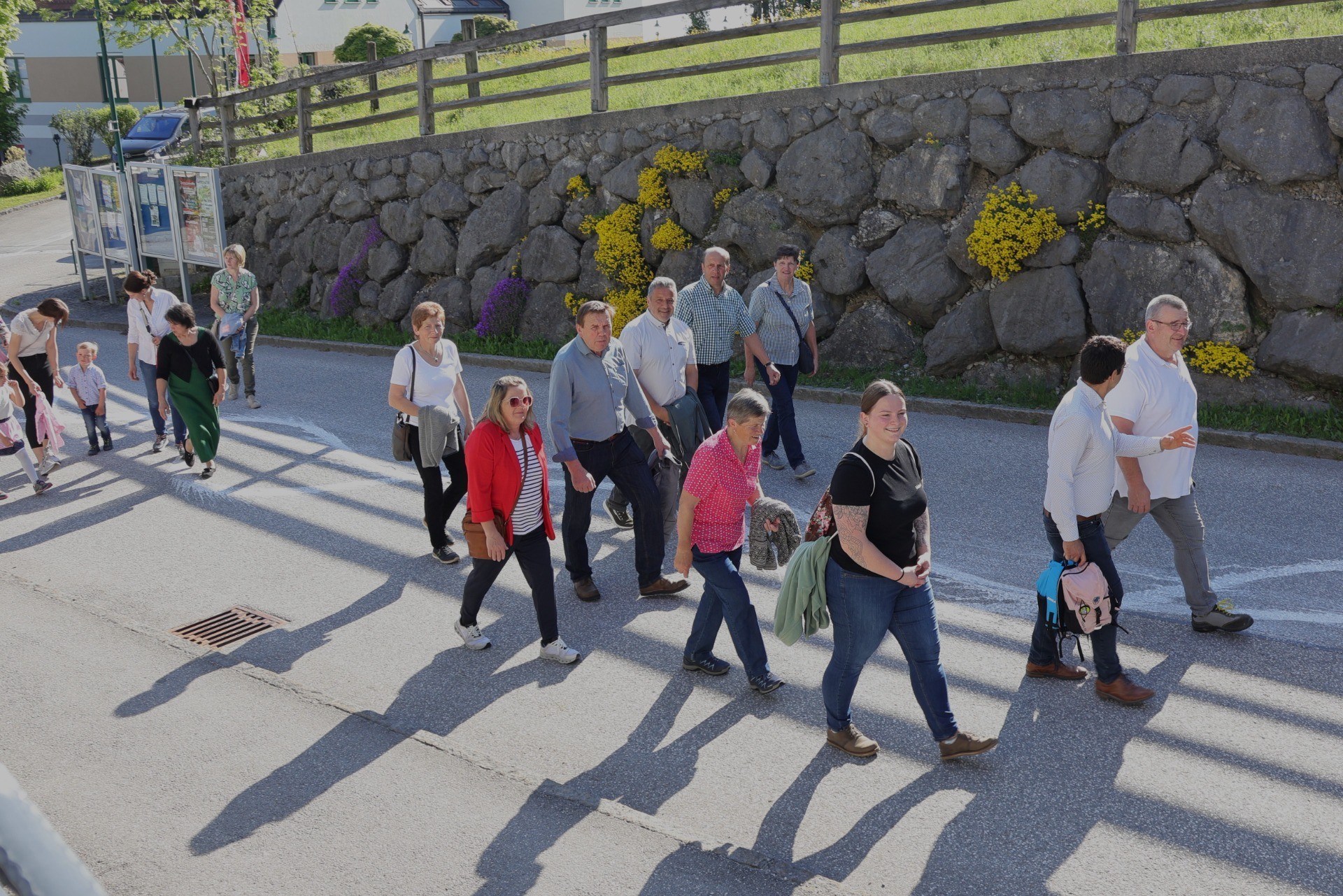 Eine Gruppe von Menschen geht auf einer belebten Straße, Schatten fallen von den Gebäuden.