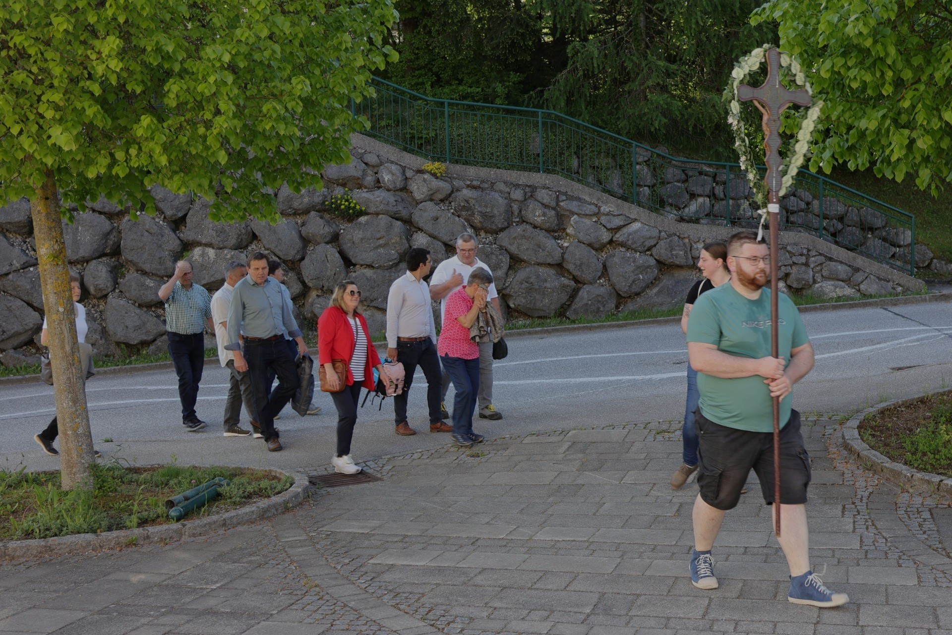 Eine Gruppe von Menschen geht auf einem Pflasterweg in einer Parkanlage. Im Hintergrund befindet sich ein lockerer Felswall und ein Zaun.