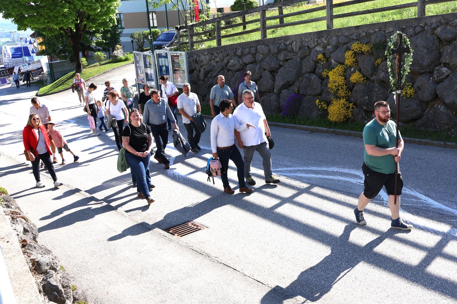 Ein Spaziergang von Personen auf einem Bürgersteig. Im Hintergrund eine Steinmauer und ein Schattenspiel.