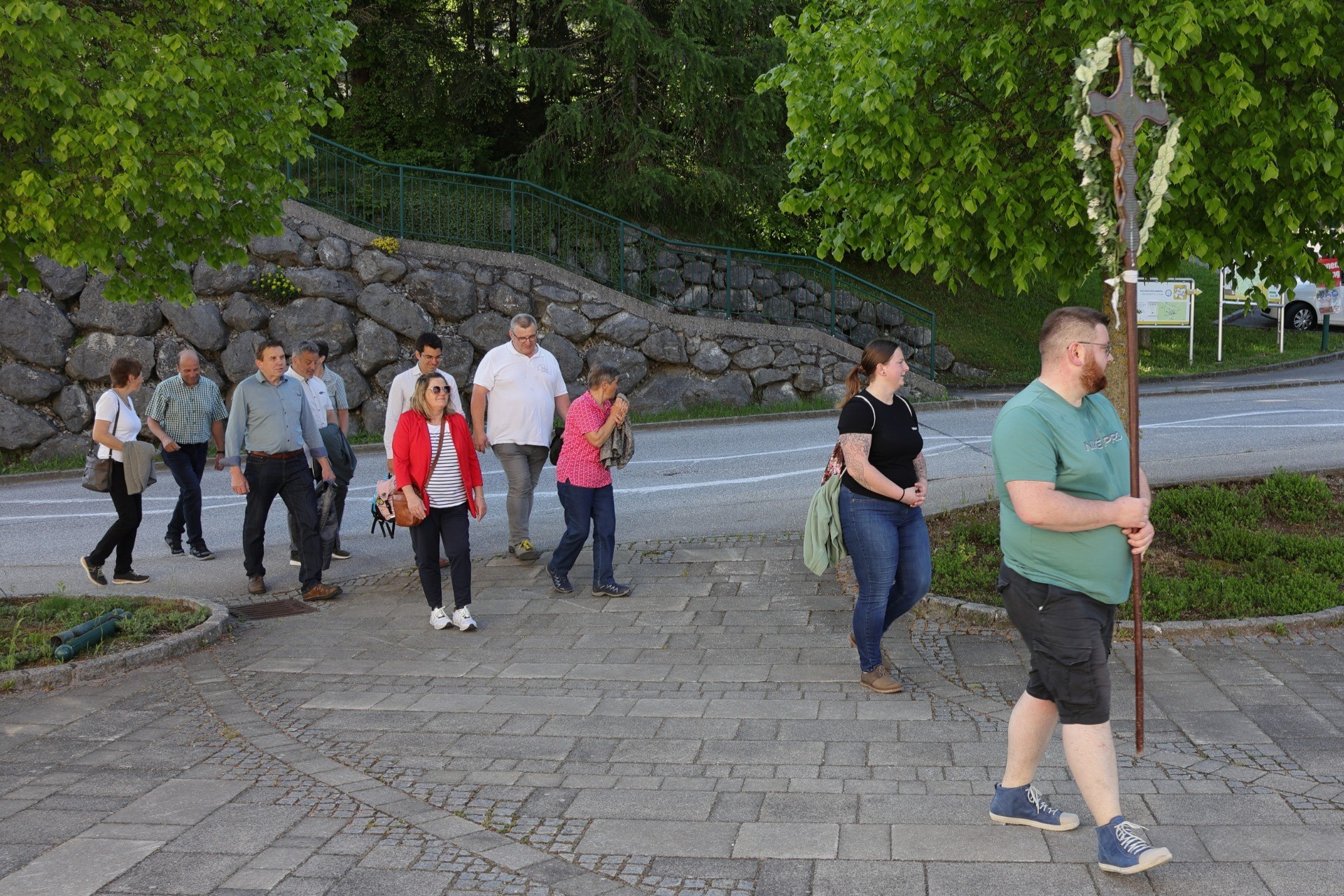 Gruppe von Menschen am Wegesrand, Schritte auf Pflaster, Steinmauer im Hintergrund.