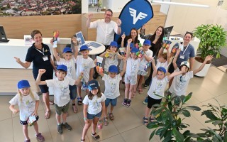 Kinder und eine Erwachsene lächeln und zeigen die Daumen hoch in einem Raum. Einige tragen Mützen und haben Spielzeug in der Hand.