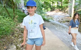 Eine junge Frau mit blauem T-Shirt und Jeans steht im Wald, umgeben von Bäumen.