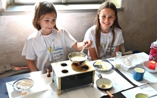 Zwei Kinder backen zusammen an einem Tisch. Sie arbeiten an einem einfachen Rezept, vermutlich Kuchen oder Muffins.