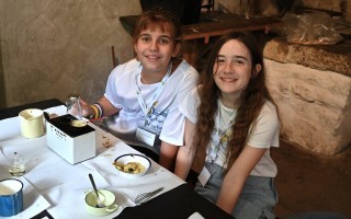 Zwei Kinder sitzen an einem Tisch mit einer Schale mit Masse, einer Kugel und einem Schneebesen.