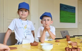 Zwei Kinder formen mit Ton. Auf einem Tisch stehen Tonstücke und eine Tonwanche.