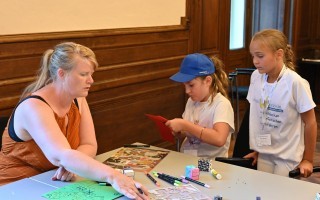 Eine Frau hilft einer jungen Frau beim Basteln an einem Tisch mit Stiften, Papier und Bauklötzen.