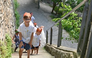 Kinder steigen eine Steinmauerweg mit Geländer und Treppen hinauf, tragen rote Armbänder und T-Shirts.