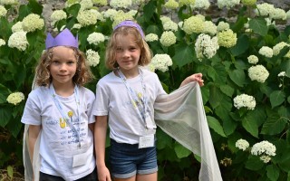 Zwei Kinder im Schuluniform mit gelbem Smiley, vor einem Hintergrund aus weißen Blüten.