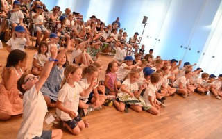 Kinder sitzen in einem Raum und schauen auf etwas emsig. Einige heben die Hände.