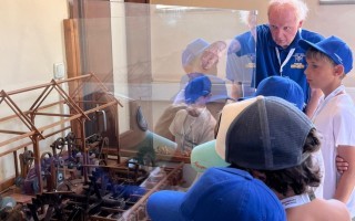 Ein älterer Mann erklärt Kindern, die einen mechanischen Vogel an einem transparenten Flügelmodell betrachten.