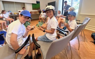 Kinder sitzen an einem Tisch und spielen mit Kartenspielen. Es sind mehrere Kinder in einem Raum zu sehen.