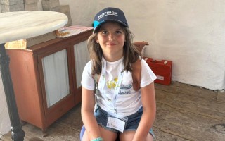 Ein Mädchen mit Sommersprossen, Schuluniform und gelbem Armband lächelt in die Kamera.