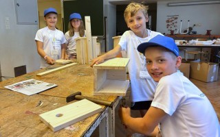 Kinder bauen gemeinsam einen Holzrahmen an einem Tisch in einem Werkraum.