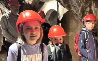 Kinder mit orangefarbenen Helmen stehen in einem dunklen Raum, vermutlich bei einer Tour oder einem Ausflug.