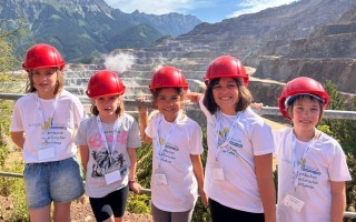 Mehrere Kinder mit Bauhelmen stehen zusammen, wahrscheinlich auf einer Baustelle.