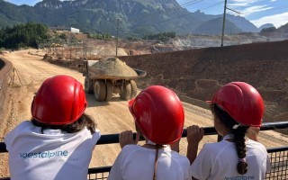 Drei Bauarbeiter mit roten Schutzhelmen blicken über eine Baustelle mit einem Radlader.